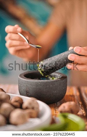 Soft focus of crop female adding spoonful of olive oil to mortar with mojo de cilantro sauce while cooking papas de tenerife dish for lunch