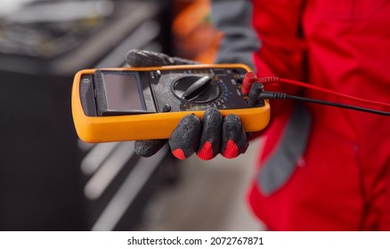 Soft focus of crop male technician using multimeter to measure voltage of car battery while working in garage