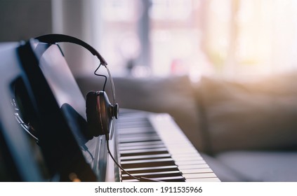Soft focus Digital Piano keyboard with Modern Headphones for music with blurry of sofa background, Cosy cinematic scene of relaxing in living room with morning light shining through window