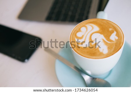 Soft focus effect. Top view of aroma coffee with adt on milky top foam in ceramic blue mun on working place nale laptop computer and smartphone, from above image of caffeine cappuccino for refreshment