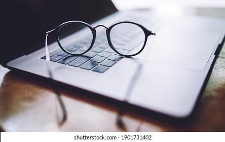 Soft focus of eyeglasses left by worker on keyboard of opened modern laptop with black screen after doing work task