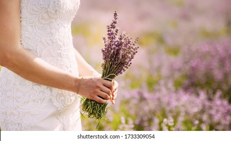 Soft focus. The girl in a white wedding dress holds a bouquet in a lavender field. Delicate pink warm color in the photo. Hand close-up. Lavender Paradise Wedding - Powered by Shutterstock