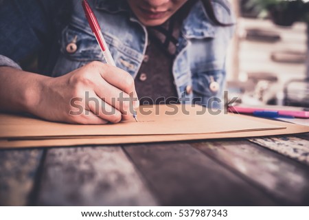 soft focus hands of a young woman as she is writing letter and notepad Or something on a wooden table . Customize colors Vintage retro and old film Tone .