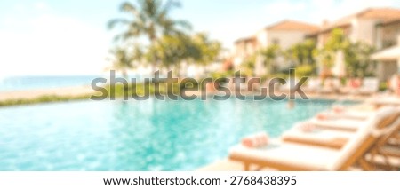 A soft focus image capturing the serene ambiance of a luxury resort swimming pool, overlooking the ocean with lush palm trees and buildings in the background.