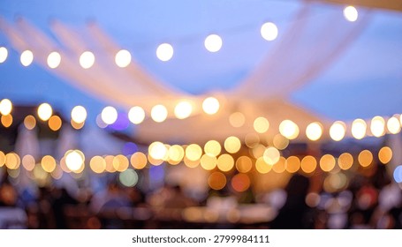Soft focus image of numerous warm string lights illuminating an outdoor gathering at dusk, creating a festive and magical atmosphere.