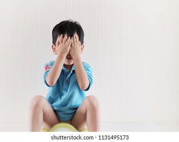 Soft Focus At Little Asian Boy Sitting On The Potty Suffering From Stomach Ache. The Kid Covering His Face With Hands While Sitting On Potty. Copy Space And Toilet Training Concept.