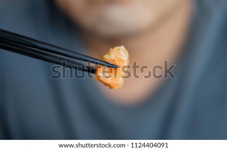 Soft focus Man hand use chopsticks tong Salmon spicy salad in Thai and japan fusion food style with burr background.