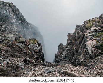 Soft focus. Mountain view from cliff at high altitude. Mystical landscape with beautiful sharp rocks near precipice and couloirs in low clouds. Mountain foggy scenery on abyss edge with sharp stones.