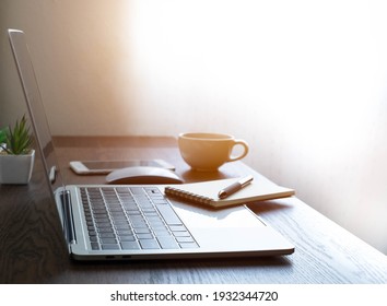 Soft Focus Of Office Desk Table With Keyboard Of Laptop Computer, Coffee Cup And Notebook, Glasses. Business And Finance Concept. Workplace With Morning Sunlight From Window With Copy Space.