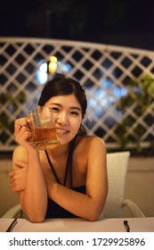 Soft focus on the background and a close-up of a smiling Japanese woman sipping a beer in a restaurant at night