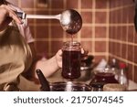 Soft focus on a ladle and a glass jar in the hands of a housewife, a confectioner pouring freshly made cherry jam into a sterile jar in a home kitchen. Woman preparing homemade canned food