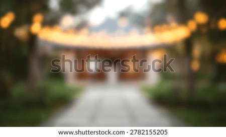 A soft focus outdoor scene features a garden walkway leading toward a building decorated with glowing string lights in the evening.