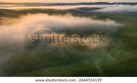 Soft focus. Panoramic landscape with thick morning clouds over a hilly valley, sunrise time. Aerial view.