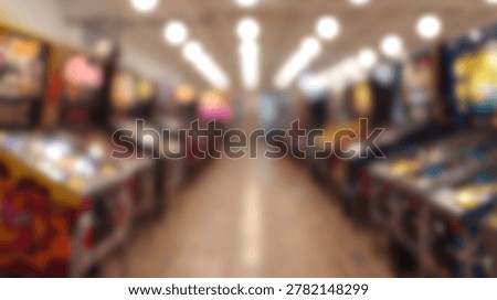 A soft focus perspective of multiple pinball machines arranged in rows within a dark indoor arcade environment featuring overhead lighting