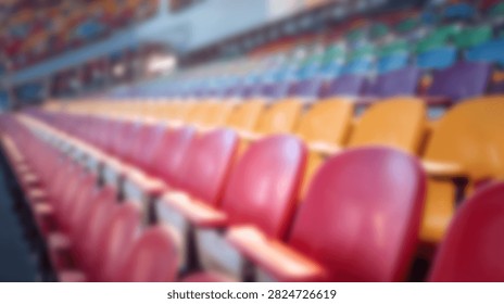 A soft focus perspective of rows of red yellow and blue plastic chairs inside a vacant indoor stadium or auditorium during an event break