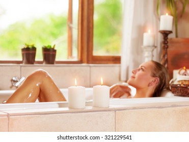 Soft Focus Photo Of Gentle Young Woman Lying Down In Bath Tub With Foam And Candle, Enjoying Spa Procedure In The Luxury Resort
