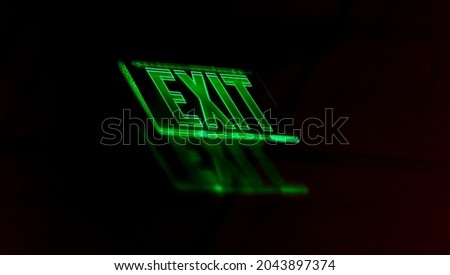 Soft focus reflection of illuminated green neon exit sign on a shinny black surface.