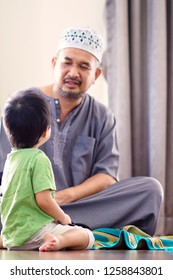 Soft focus of religious 40s Asian Muslim Man teaching his little 2 years old son to pray to God at home.They were wearing prayer cap.Peaceful and Marvelous warm climate.Selective focus