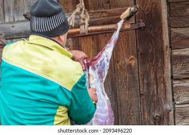 Soft Focus. Street Lighting. A Man With A Knife Removes The Skin From A Dead Animal. Rural Area