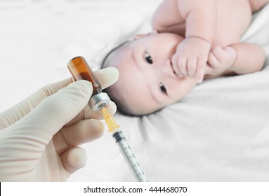 Soft Focus Syringe With Vial On Hands Of A Nurse,doctor Administer The Injection And Blurred Background Of  Infant Asian Baby On The Towel.