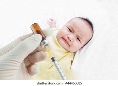 Soft Focus Syringe With Vial On Hands Of A Nurse,doctor Administer The Injection And Blurred Background Of  Infant Asian Baby On The Towel. The Baby Boy Is Scared. 