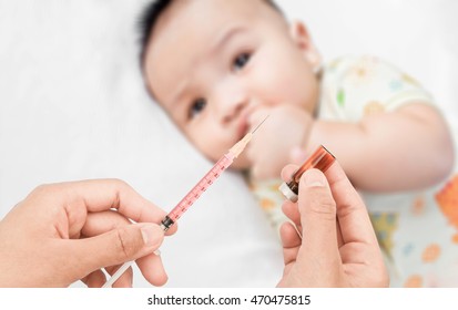 Soft Focus Syringe With Vial On Hands Of A Nurse,doctor Administer The Injection And Blurred Background Of Infant Asian Baby On The Towel.