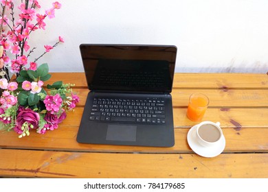 soft focus top view notebook laptop with white cup of coffee and orange juice on wood background.