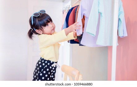 Soft Focus Of A Two Years Old Child Choosing Her Own Dresses From Kids Cloth Rack