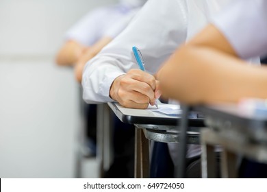 soft focus undergraduate student holding pencil and sitting on row chair doing final exam attending in examination room or classroom.university student in uniform.