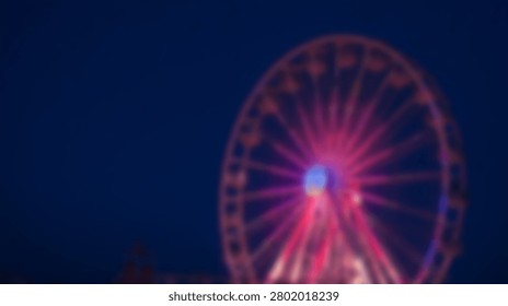 Soft focus view of a large amusement park Ferris wheel glowing with pink lights against a dark night sky