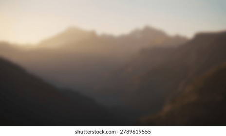 A soft focus view of a mountain range during sunrise with golden light hitting the peaks and dark shadows filling the valley in a natural setting
