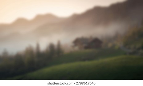 A soft focus view of a rustic cabin situated on a green slope with dense fog rolling over distant mountain peaks in the early morning light