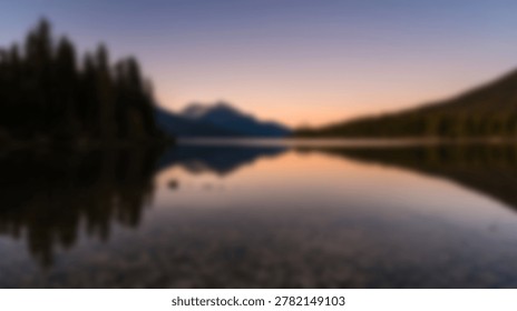 A soft focus view of a tranquil mountain lake surrounded by pine trees during a golden hour sunset with a clear reflection visible on the still water surface