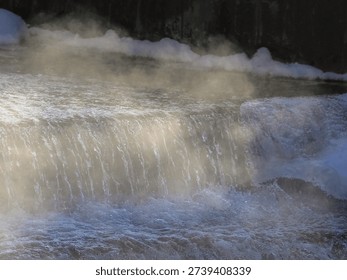 Soft focus. A waterfall is shown with steam rising from it. The weather is cold and the water is warm.. The water is cold and the steam is rising from it