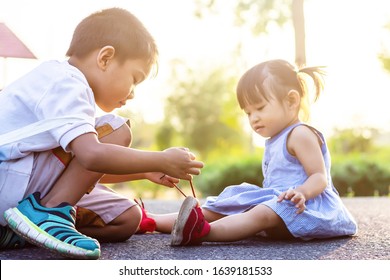 Soft focus. A young Asian brother help his little sister to tie her shoelaces. At the garden park in sunshine day summer season. Love and family concept. - Powered by Shutterstock