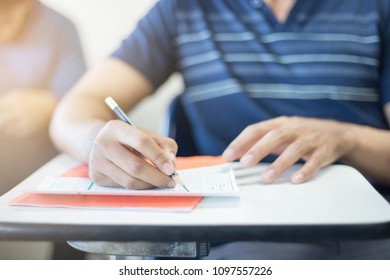 soft focus.hand high school or university student in uniform holding pencil writing on paper answer sheet.sitting on lecture chair taking final exam or study attending in examination room or classroom - Shutterstock ID 1097557226