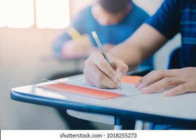 Soft Focus.high School Or University Student Holding Pencil Writing On Paper Answer Sheet.sitting On Lecture Chair Taking Final Exam Attending In Examination Room Or Classroom.student In Uniform