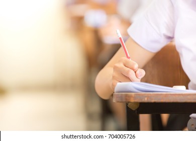 soft focus.high school or university student holding pencil writing on paper answer sheet.sitting on lecture chair doing final exam attending in examination room or classroom.student in uniform. - Shutterstock ID 704005726