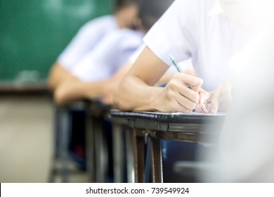 Soft Focus.high School Or University Student Holding Pencil Writing On Paper Answer Sheet.sitting On Lecture Chair Taking Final Exam Attending In Examination Room Or Classroom.student In Uniform.