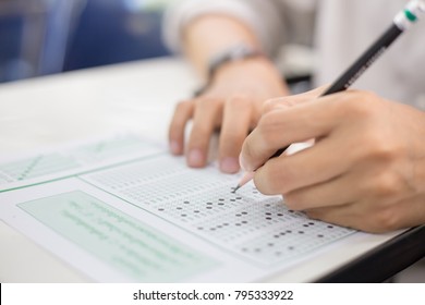 Soft Focus.high School Or University Student Holding Pencil Writing On Paper Answer Sheet.sitting On Lecture Chair Taking Final Exam Attending In Examination Room Or Classroom.student In Uniform