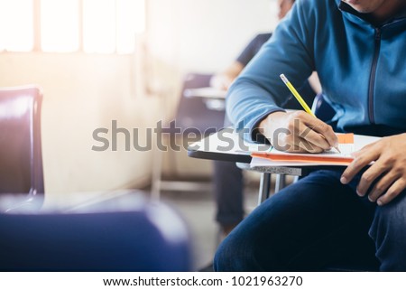 soft focus.high school or university student holding pencil writing on paper answer sheet.sitting on lecture chair taking final exam attending in examination room or classroom.student in uniform