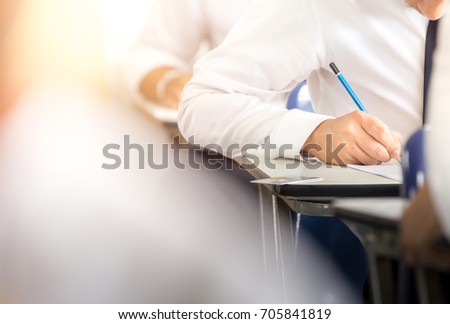 soft focus.high school or university student holding pencil writing on paper answer sheet.sitting on lecture chair doing final exam attending in examination room or classroom.student in uniform.