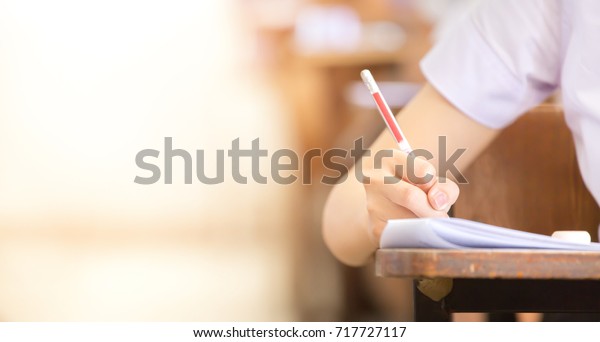 soft focus.high school or university student\
holding pencil writing on paper answer sheet.sitting on lecture\
chair taking final exam attending in examination room or\
classroom.student in\
uniform.