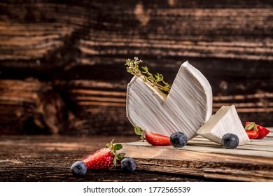 Soft French cheese with white mold, grade brie, lies on a wooden surface surrounded by blueberries and strawberries. - Powered by Shutterstock