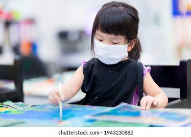 Soft Fucus. Asian Girl Wearing Cloth Face Mask While Taking Art Classes In Class. Little Child Painted Watercolor On Canvas. Children Wears Black Apron. Kids Have Fun With Crafts. Baby Is 4 Years Old.