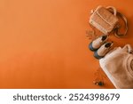 A soft, fuzzy bag, beige ankle boots, and warm knitted blanket on an orange background, accented by dried leaves, acorns, and pinecone.