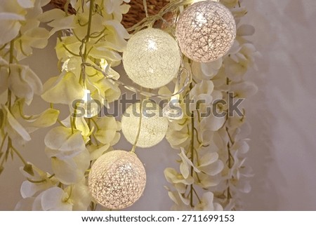 Soft glowing string lights intertwined with delicate white blossoms create a warm, elegant and festive ambiance, capturing a serene decorative moment filled with gentle luminosity and texture.