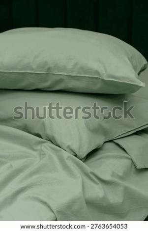 Soft green bedding set featuring stacked pillows and wrinkled sheets on a bed, creating a cozy and inviting atmosphere in a bedroom