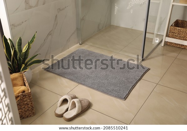 Soft grey\
bath mat and slippers on floor in\
bathroom