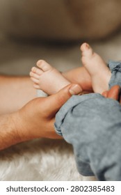 Soft hands cradle tiny feet. Gentle touch feels warm and caring. Newborn's feet curl slightly. Cozy blanket beneath delicate skin. Parent's hands hold tenderly. Perfect for parenting, family
